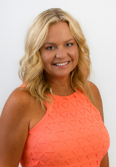 Professional headshot of Jill Whittaker smiling in a bright coral dress against a clean white background.