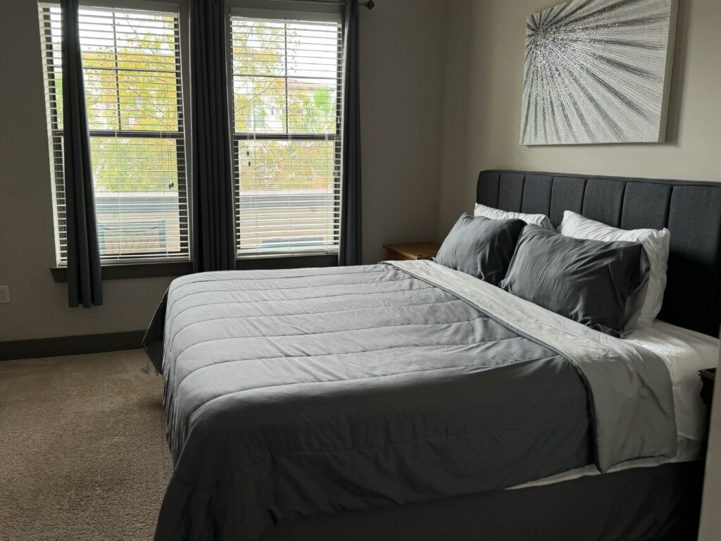 Primary bedroom at The Addison featuring a king-size bed, upholstered headboard, large windows with natural light, and modern furnishings.