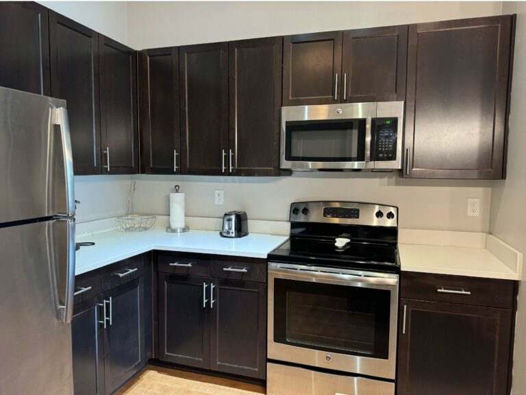 Modern kitchen at The Addison featuring stainless steel appliances, dark wood cabinetry, spacious countertops, and a fully equipped cooking area.