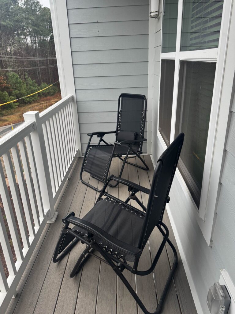 Private apartment balcony featuring two comfortable reclining lounge chairs, durable composite decking, and peaceful wooded views, offering a quiet outdoor space to relax and enjoy fresh air.