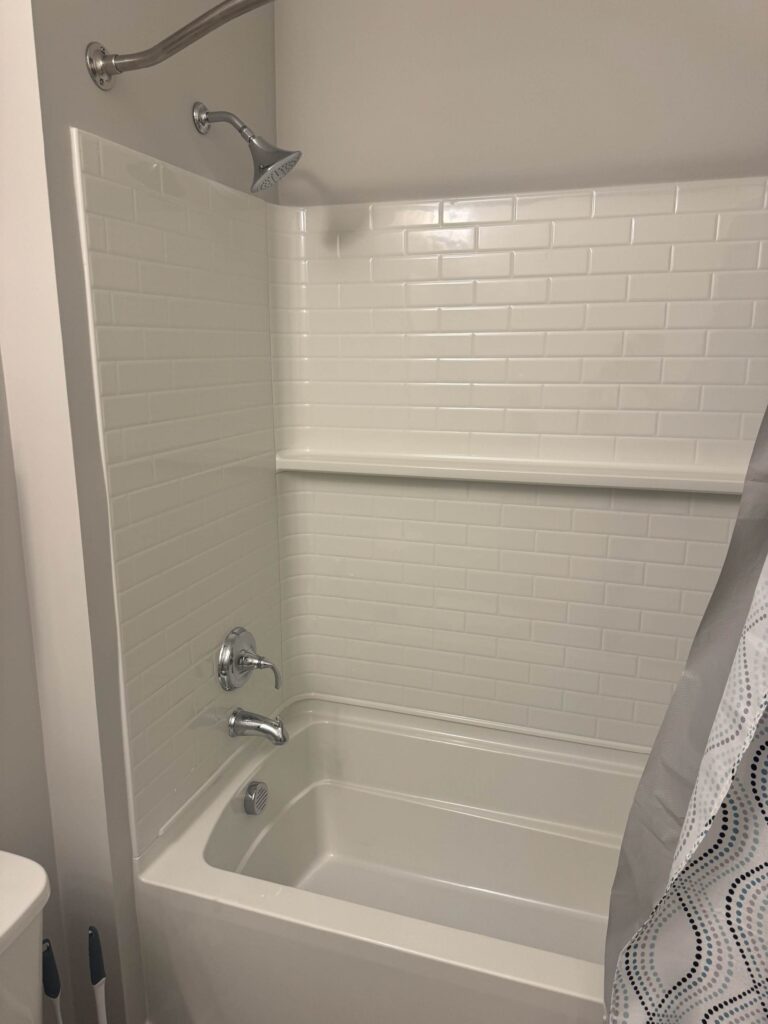 Modern bathroom featuring a full tub and shower combination with white subway tile surround, chrome fixtures, built-in storage ledge, and a clean, contemporary design.