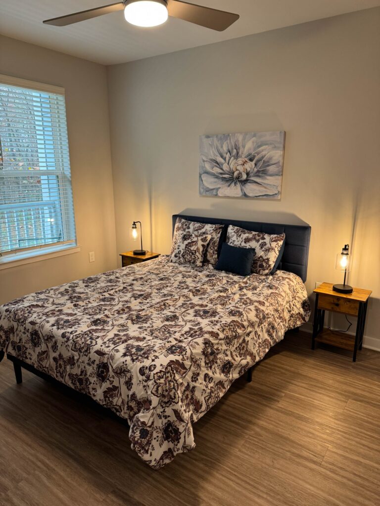 Elegant guest bedroom featuring a king-size bed with patterned bedding, modern accent lighting, ceiling fan, large window for natural light, and contemporary furnishings designed for comfort and relaxation.
