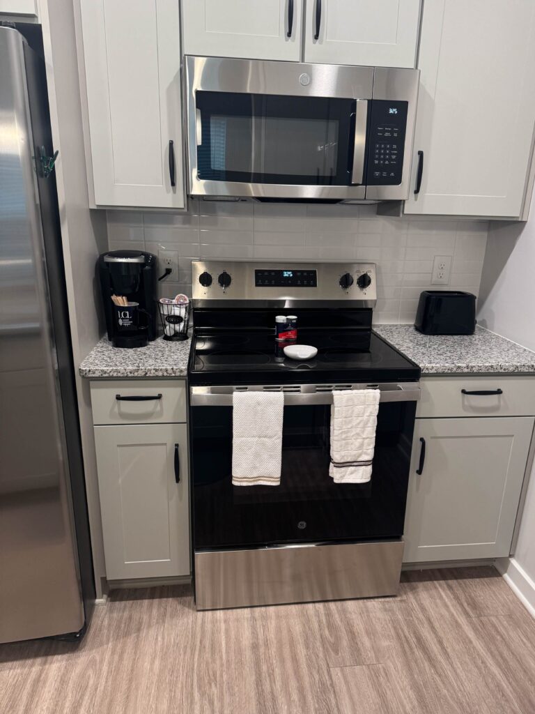 Modern kitchen at Alexander Crossing featuring stainless steel appliances, granite countertops, white shaker cabinets, a full-size oven and microwave, coffee station, and ample workspace for everyday cooking and dining.