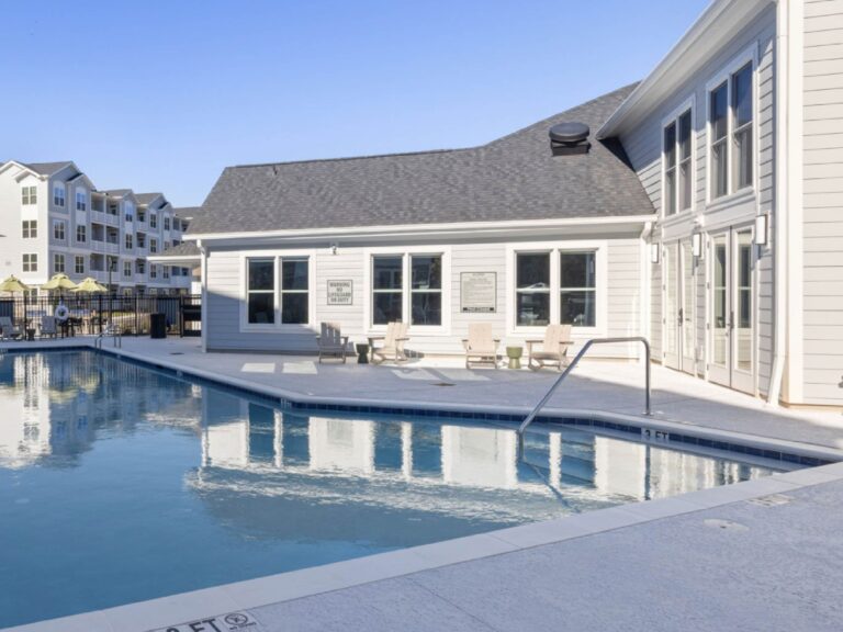 Resort style swimming pool at Alexander Crossing featuring a spacious sun deck, comfortable lounge seating, and a modern clubhouse creating a relaxing outdoor gathering space for residents and guests.