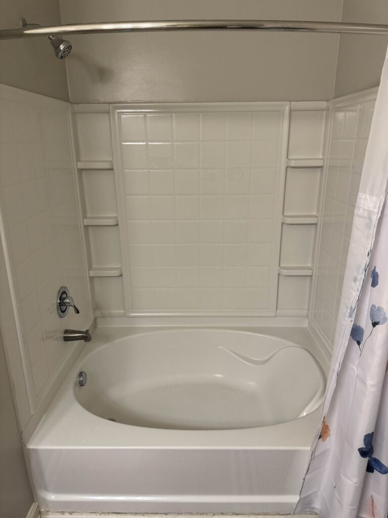 Clean bathroom featuring a full-size bathtub and shower combination with built-in shelving, modern fixtures, and a shower curtain.