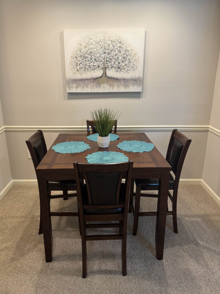 Dedicated dining area featuring a four person dining table, upholstered chairs, decorative centerpiece, and contemporary wall art.