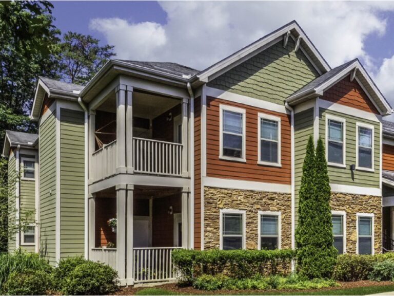 Exterior view of Audubon Place apartment homes featuring mountain-inspired architecture, covered balconies, stone accents, landscaped grounds, and mature greenery.
