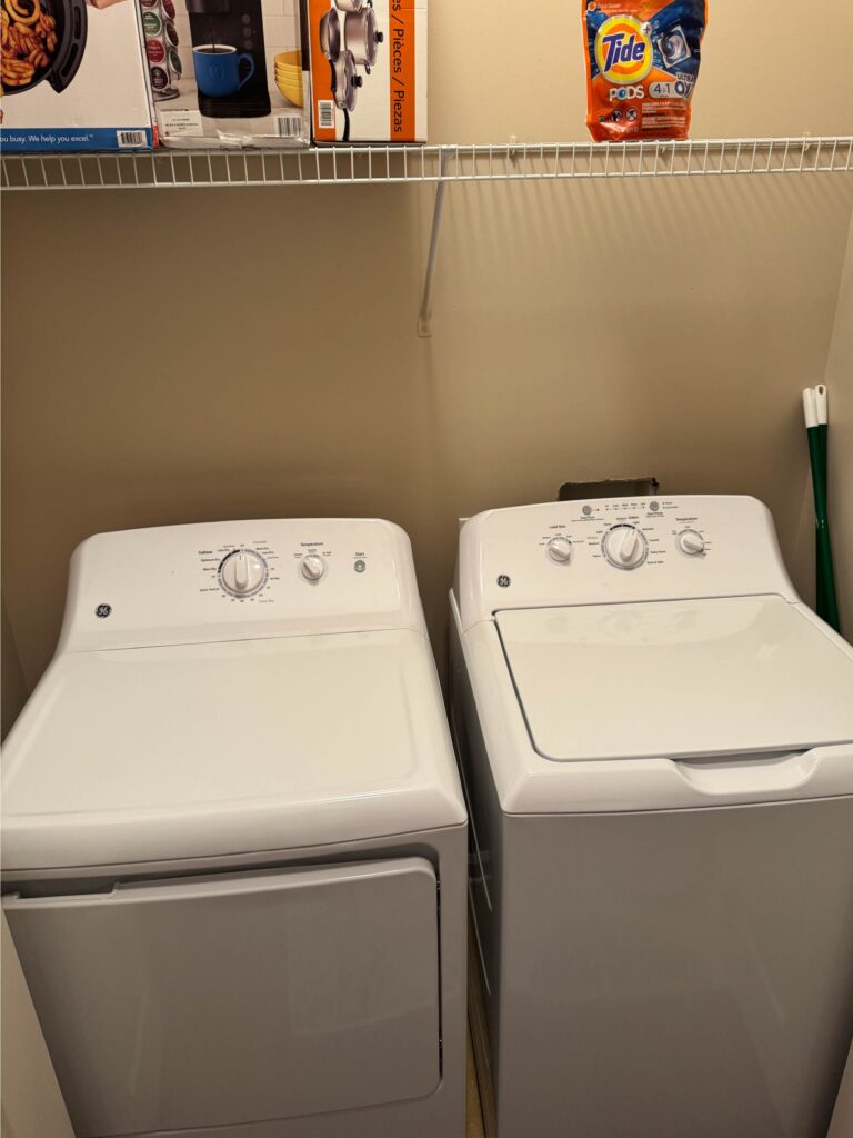Dedicated in-unit laundry area featuring a full-size washer and dryer, laundry supplies, and storage shelving.