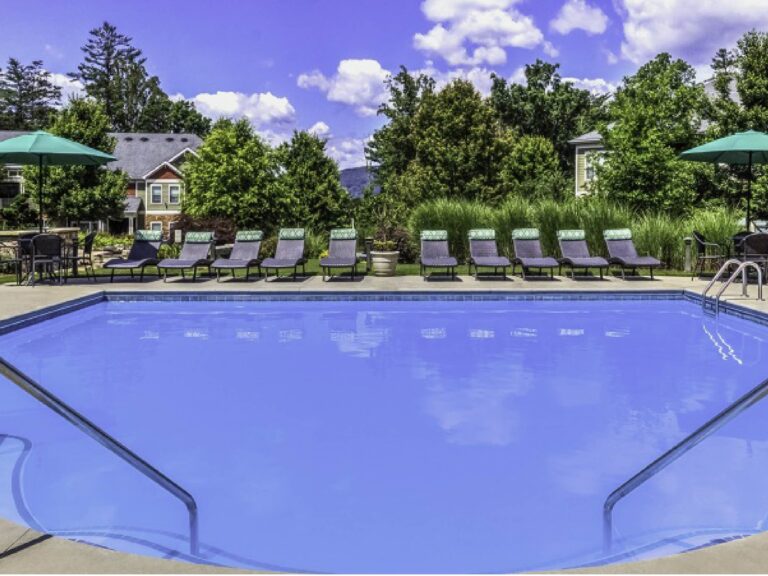 Resort-style outdoor swimming pool surrounded by lounge chairs, umbrellas, lush landscaping, and mountain views at Audubon Place in Arden, North Carolina.