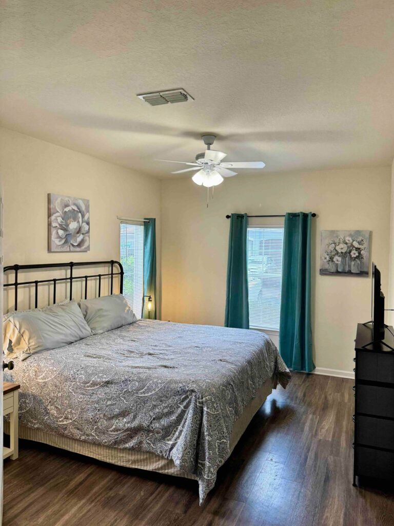 Spacious bedroom at Ballantrae Apartments in Sanford with king bed, wood style flooring, ceiling fan, and natural light
