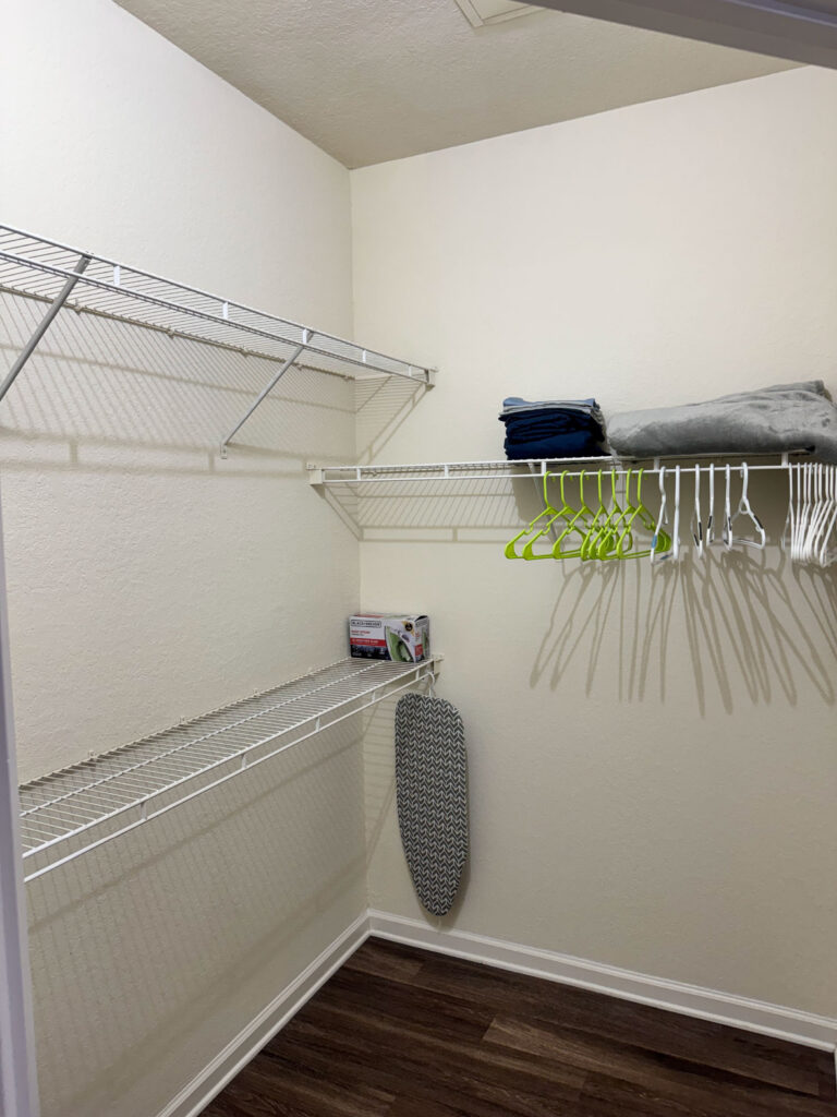 Walk in closet at Ballantrae Apartments with shelving, hanging space, linens, hangers, ironing board, and storage organization