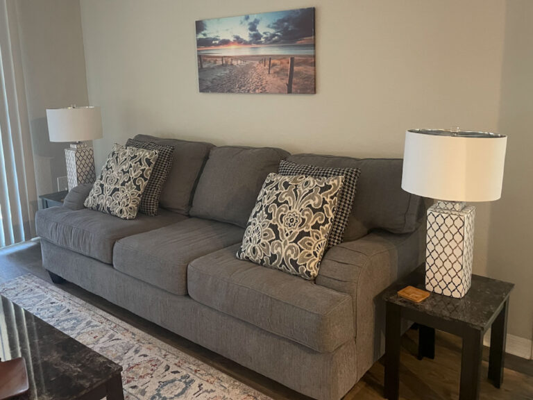 Living room at Ballantrae Apartments with gray sofa, decorative lighting, patterned accent pillows, and furnished apartment decor