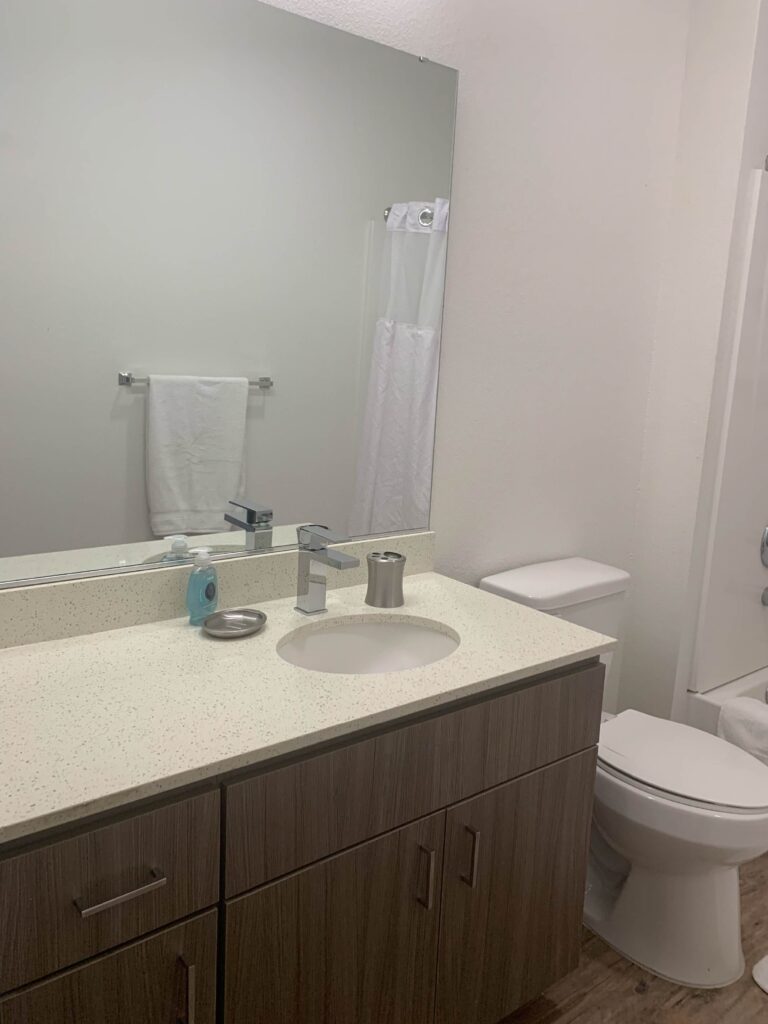 Modern bathroom at Cielo Luxury Living featuring a quartz vanity countertop, contemporary wood cabinetry, large wall mirror, and a tub/shower combination.