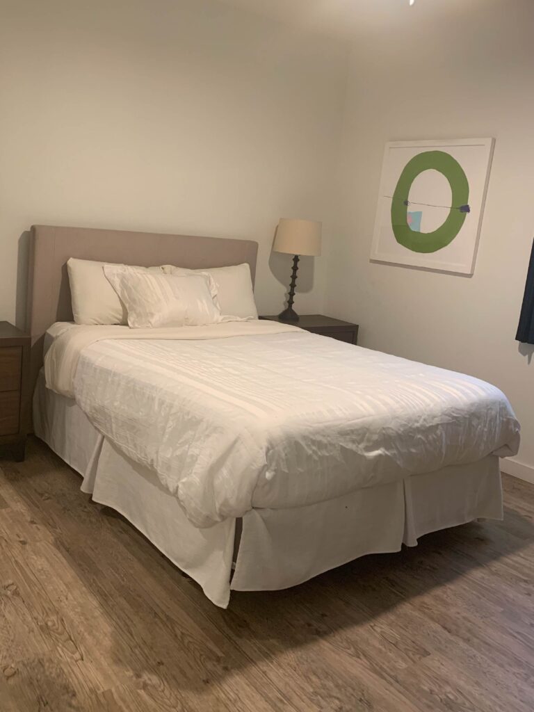 Primary bedroom at Cielo Luxury Living featuring a queen-size bed with premium linens, matching nightstands, bedside lighting, contemporary artwork, and wood-style flooring.