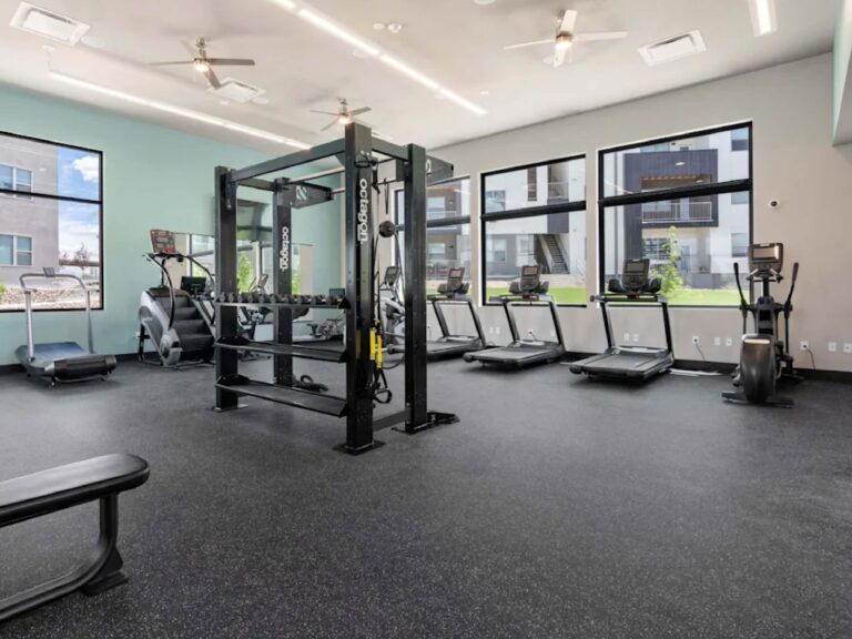 Modern fitness center at Cielo Luxury Living featuring treadmills, ellipticals, free weights, and a functional training station with floor-to-ceiling windows overlooking the community courtyard.