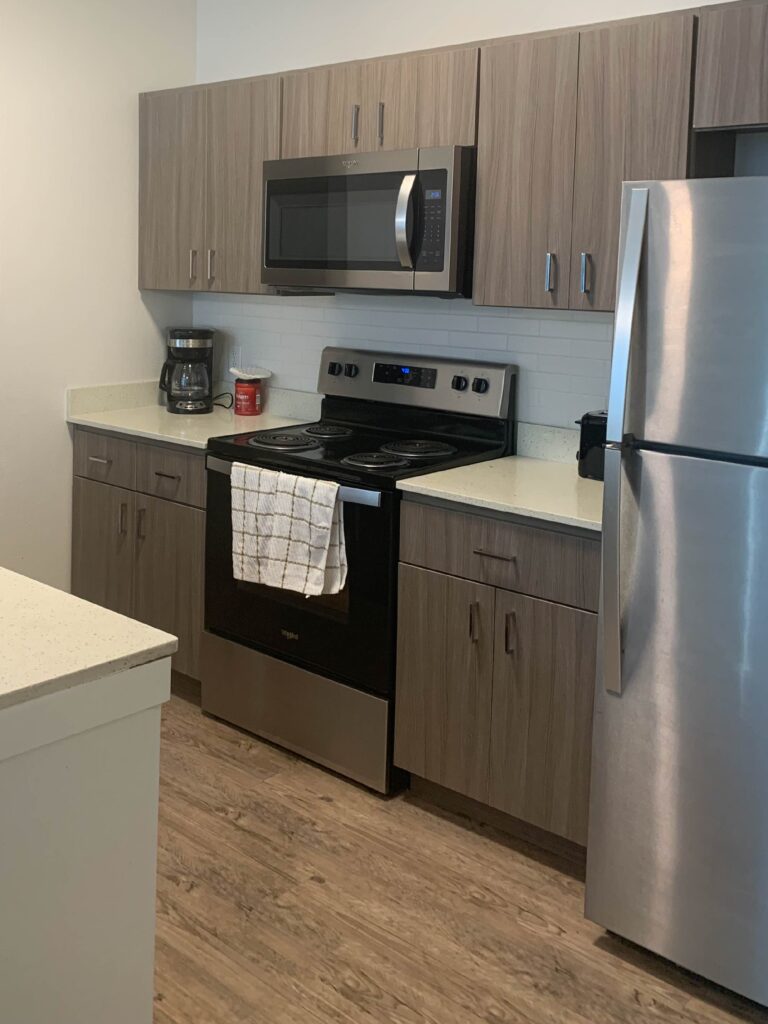 Modern kitchen at Cielo Luxury Living featuring stainless steel appliances, contemporary wood cabinetry, solid surface countertops, a full-size refrigerator, microwave, oven, and ample preparation space.