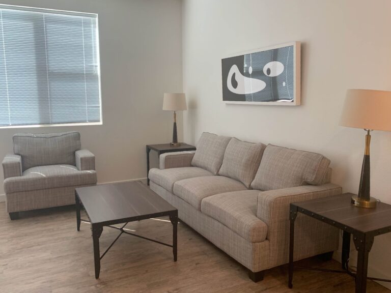 Contemporary living room at Cielo Luxury Living featuring a spacious sofa, matching armchair, coffee table, accent lighting, and modern artwork in a bright open-concept layout.