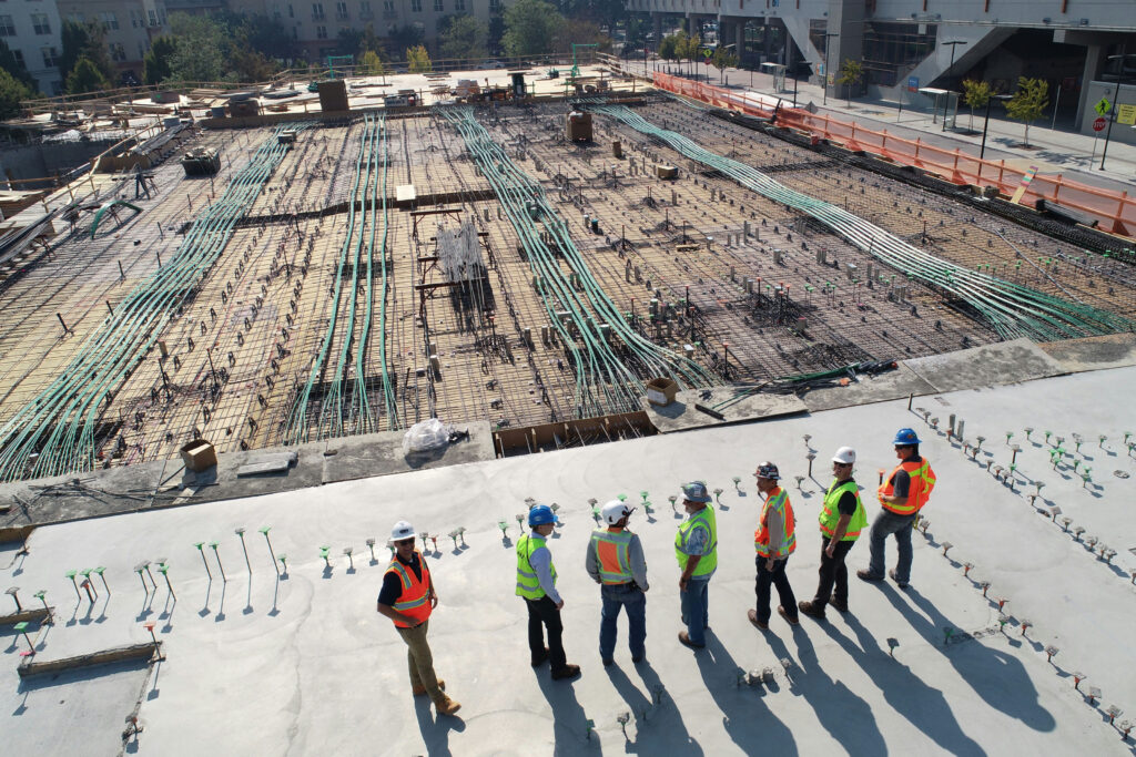 Construction and engineering professionals conducting a site inspection at a large commercial construction project with structural foundations and utility infrastructure in progress.