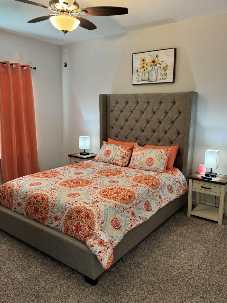 Primary bedroom at Covey Homes featuring a tufted upholstered bed, patterned bedding, bedside tables, and ceiling fan.