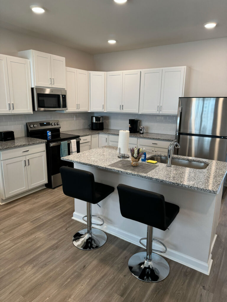 Modern kitchen at Covey Townhomes featuring white cabinetry, stainless steel appliances, granite countertops, and island seating.