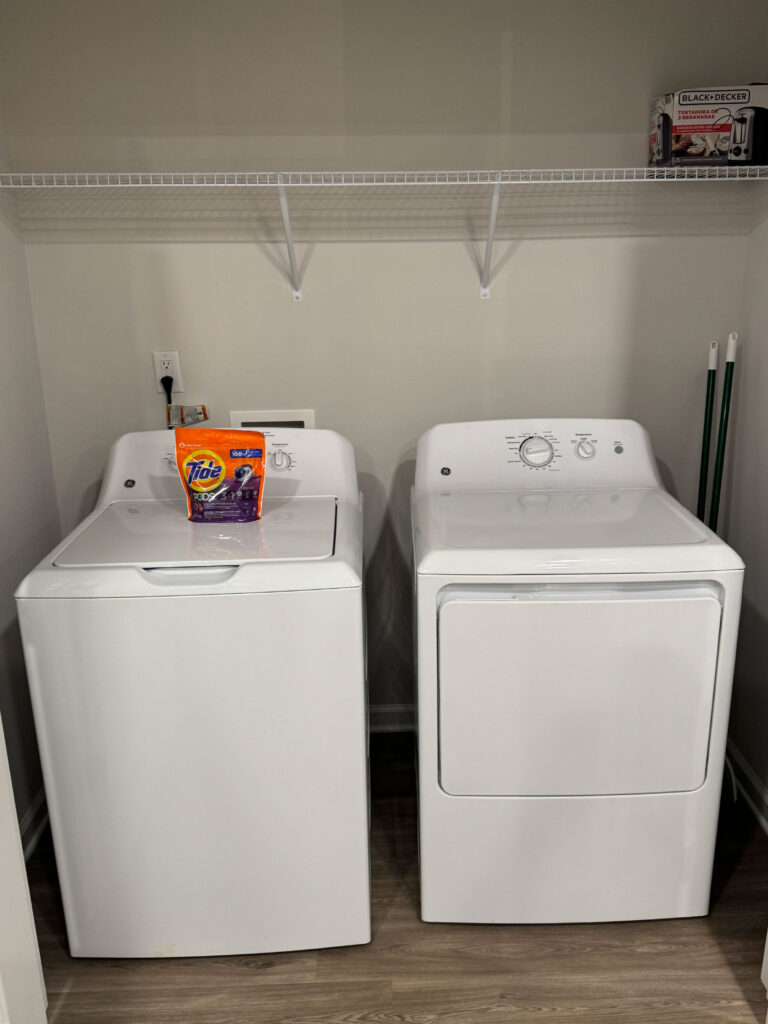 In-unit laundry area at Covey Homes with full-size washer, dryer, and storage shelving.