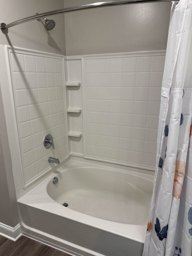 Full bathroom at Creekstone at RTP featuring a combination tub and shower, clean white surround, built in shelving, curved shower rod, and residential finishes.