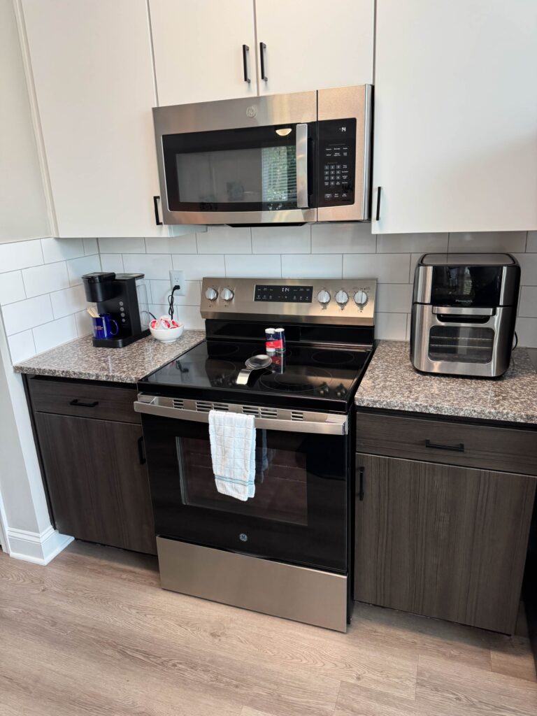 Modern kitchen at Creekstone at RTP featuring stainless steel appliances, quartz-style countertops, white cabinetry, subway tile backsplash, coffee maker, and countertop air fryer.