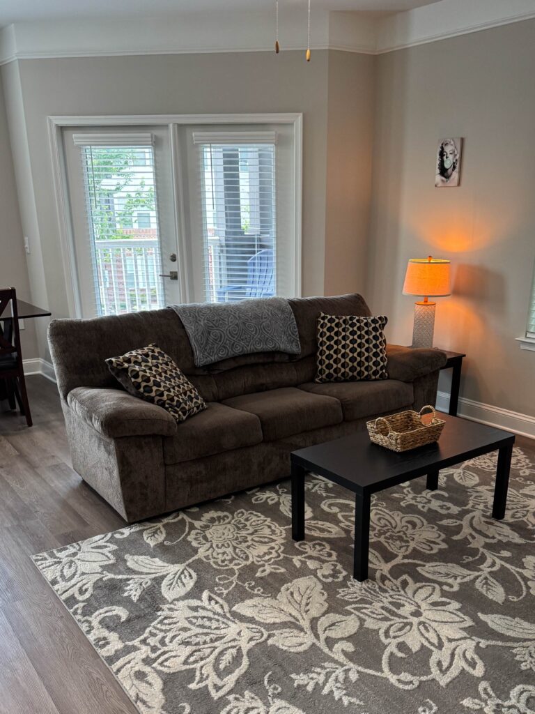 Comfortable living room at Creekstone at RTP featuring a plush sofa, decorative area rug, coffee table, accent lighting, and direct access to a private balcony.