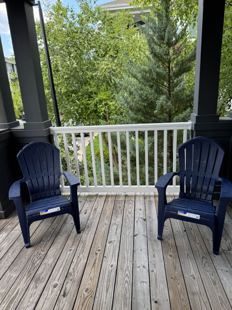 Private covered balcony at Creekstone at RTP featuring two Adirondack style chairs overlooking mature trees and landscaped community grounds.
