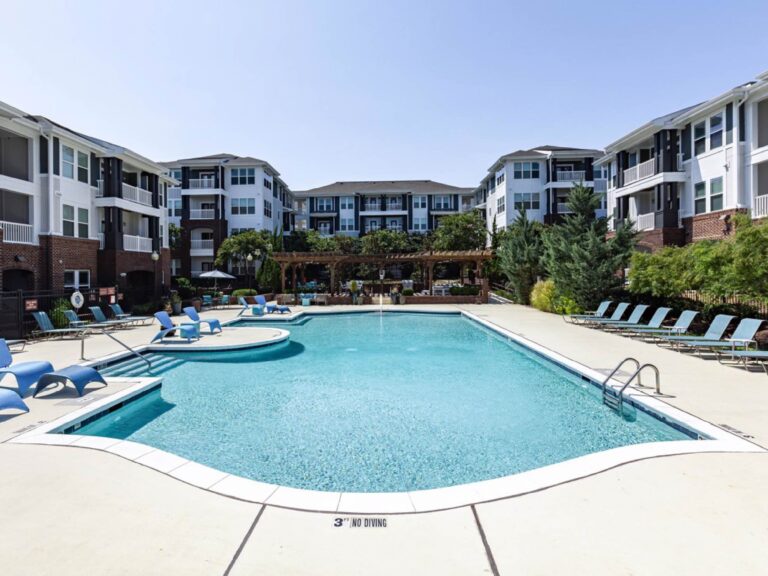 Resort style swimming pool at Creekstone at RTP featuring expansive sundecks, in water lounge chairs, shaded pergola seating, and luxury apartment residences surrounding the courtyard.