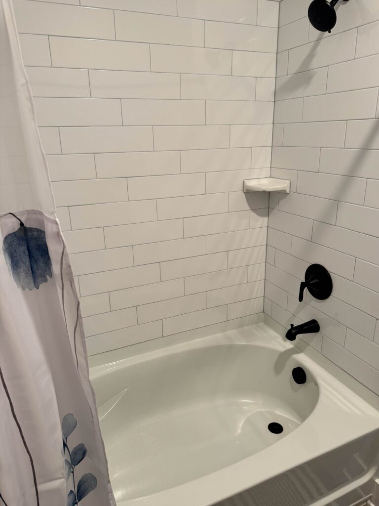 Modern bathroom featuring a deep soaking tub and shower combination with white subway tile surround, matte black fixtures, and a clean contemporary design.