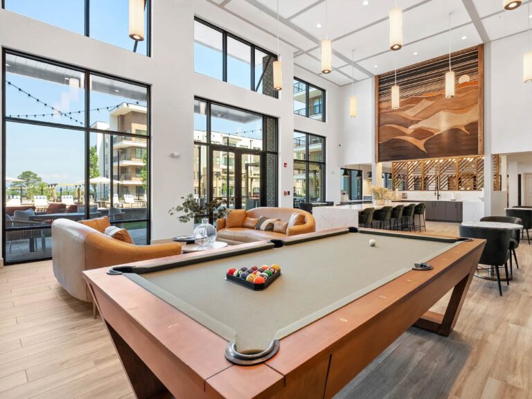 Luxury clubhouse featuring a pool table, soaring ceilings, floor-to-ceiling windows, lounge seating, social gathering spaces, and contemporary mountain-inspired design.