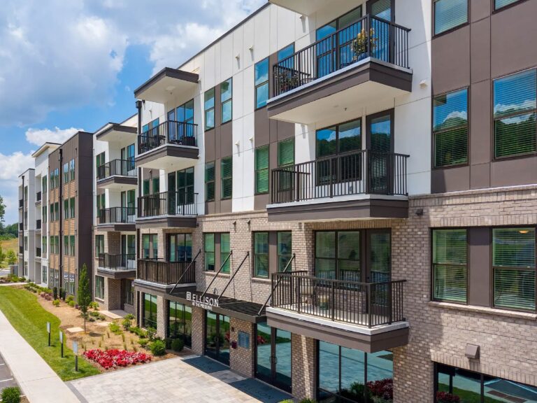 Modern multi-story apartment community featuring contemporary architecture, private balconies, large windows, landscaped grounds, and the main entrance to Ellison at the Preserve.