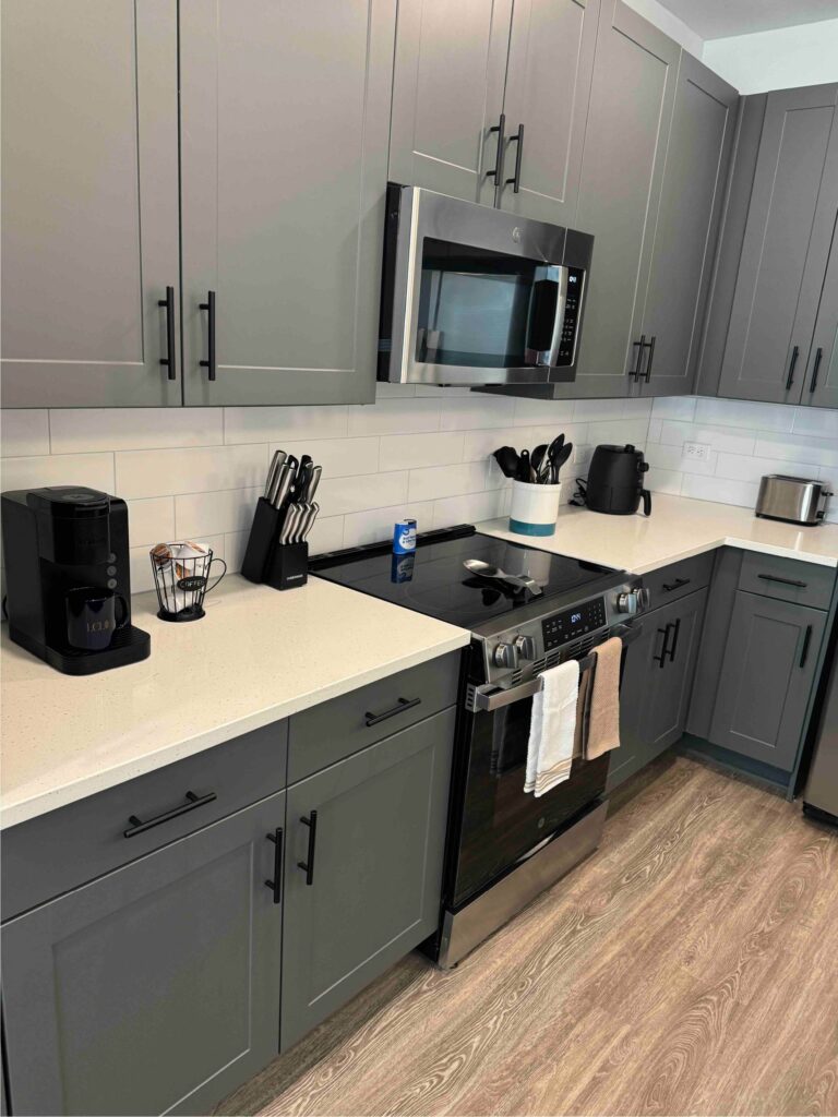 Modern kitchen featuring gray shaker-style cabinetry, stainless steel appliances, white quartz countertops, subway tile backsplash, and a fully equipped cooking station.