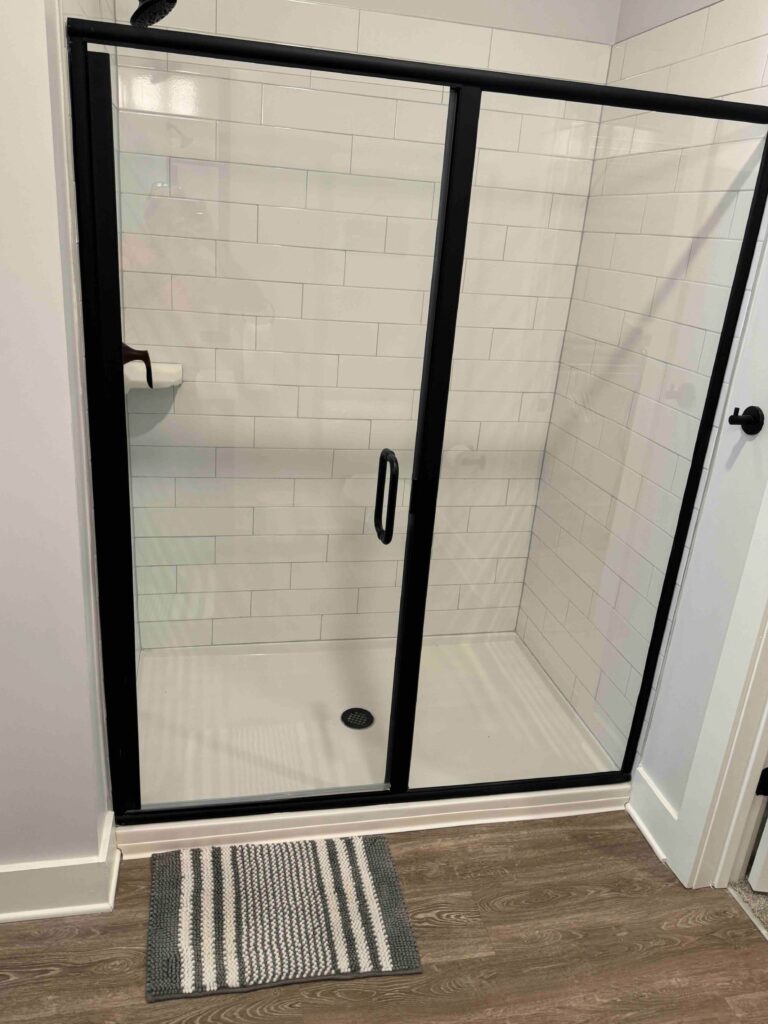 Spacious walk-in shower featuring white subway tile walls, black framed sliding glass doors, modern black fixtures, and a low-threshold entry.