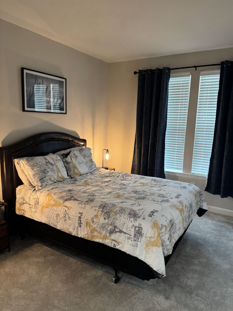 Furnished bedroom at Evergreen at Southwood featuring a queen size bed, blackout curtains, and modern decor in Tallahassee Florida