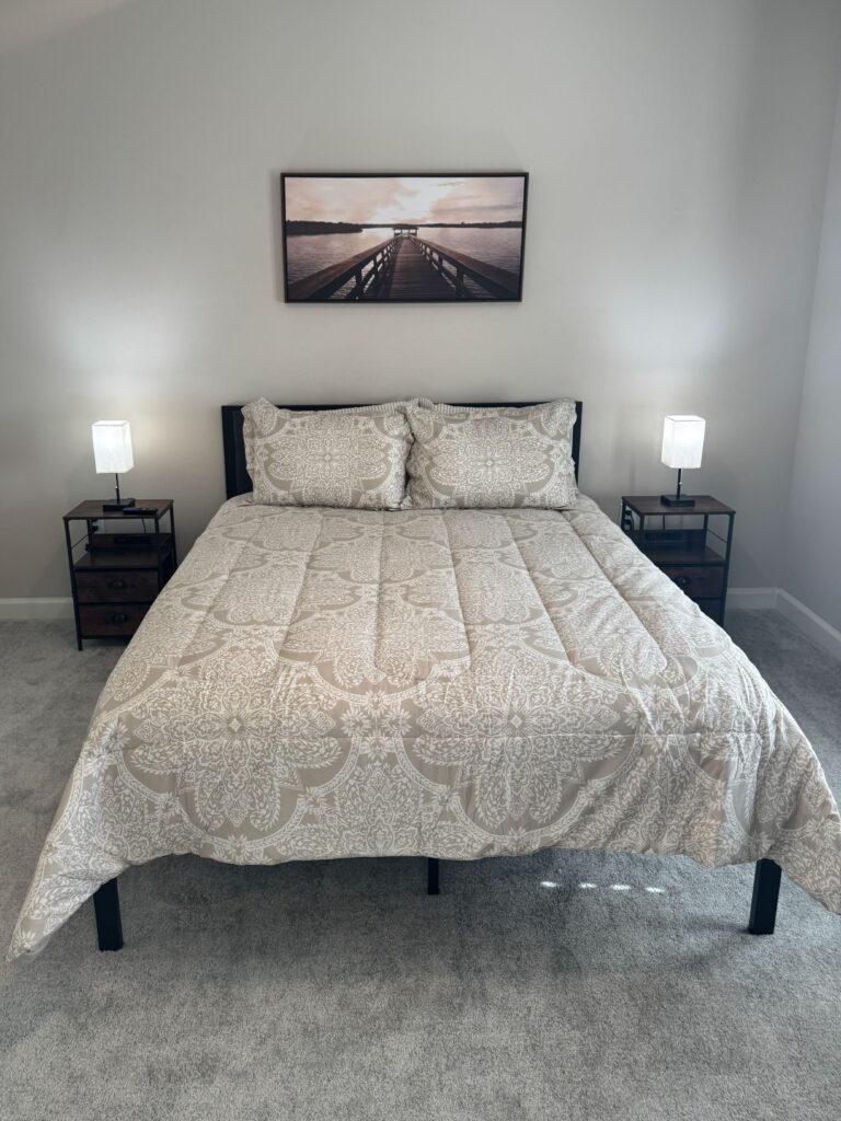 Furnished bedroom at Evergreen at Southwood featuring a queen size bed, soft carpeting, bedside lighting, and neutral decor in Tallahassee Florida