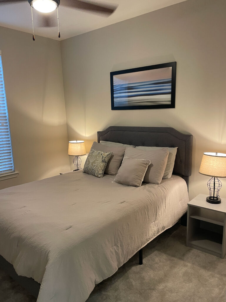 Modern furnished bedroom at Evergreen at Southwood in Tallahassee featuring a queen bed, bedside lighting, and soft neutral décor for extended stay comfort