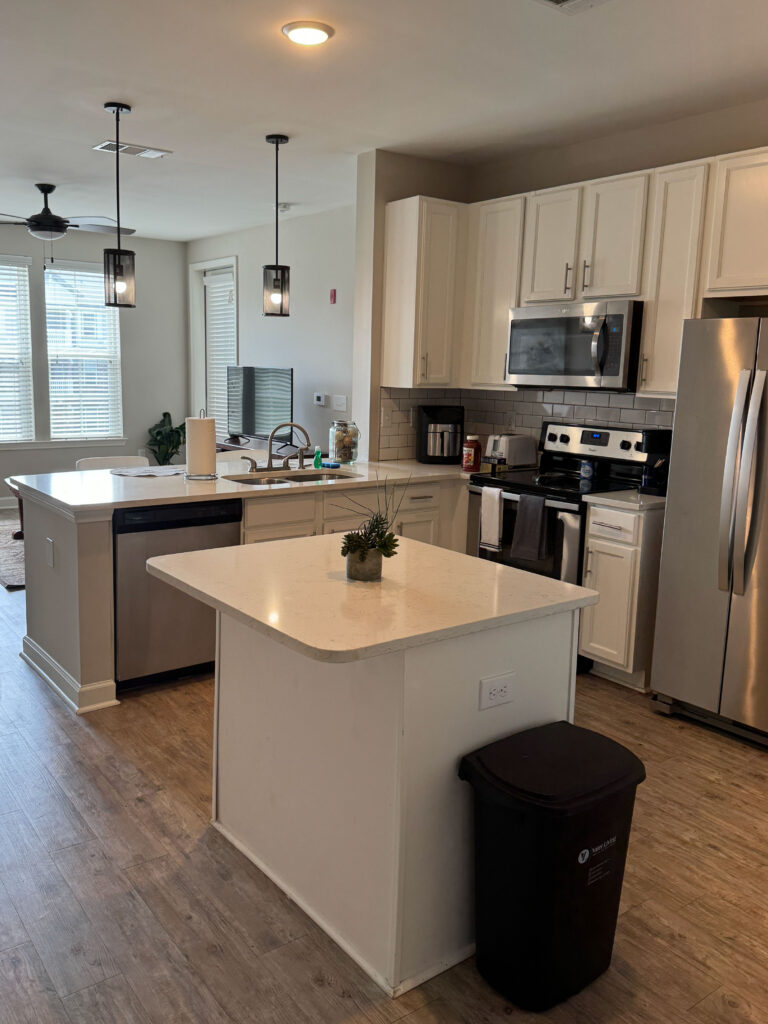 Modern open concept kitchen at Evergreen at Southwood in Tallahassee featuring stainless steel appliances, quartz countertops, and furnished extended stay living