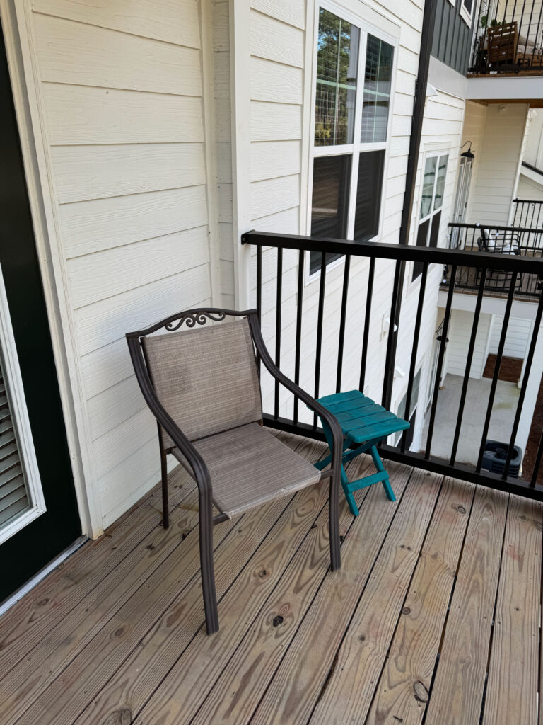 Private apartment balcony with outdoor chair, side table, wood decking, and community courtyard views.