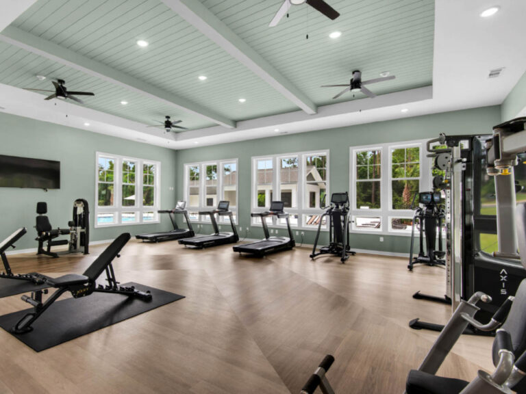 Bright modern fitness center with treadmills, weight machines, benches, and large windows overlooking the community.
