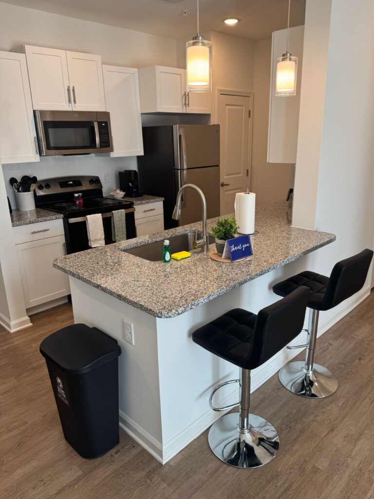 Modern furnished kitchen with granite island, pendant lighting, stainless steel appliances, and bar seating at Exchange at Blair Stone.