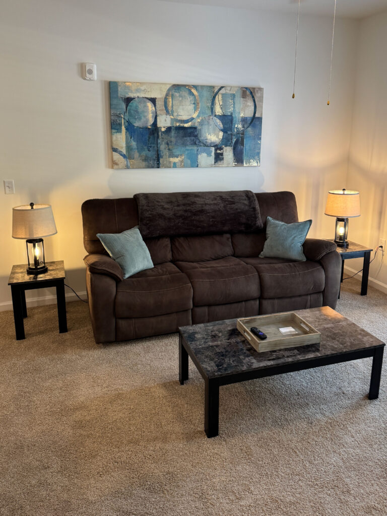 Cozy furnished living room with reclining sofa, accent lighting, wall art, and coffee table in a modern apartment.
