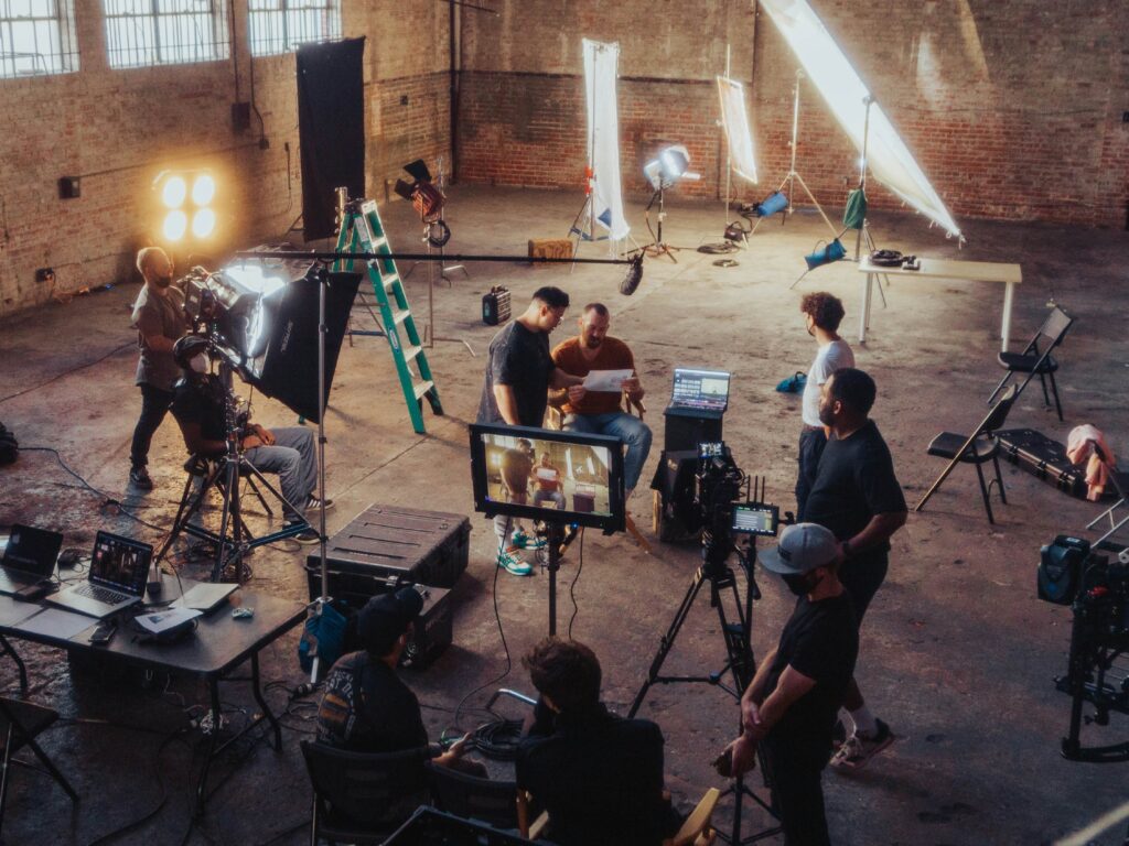 Film and media production crew working on a professional video shoot inside a studio with cameras, lighting equipment, monitors, and production staff.