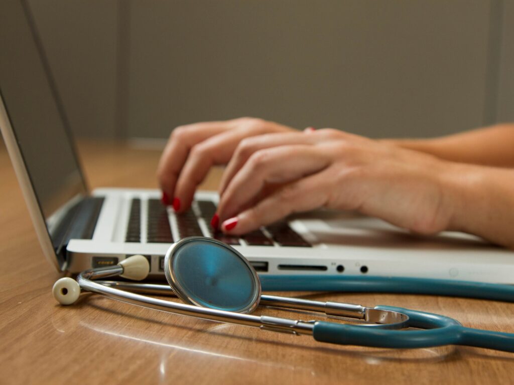 Healthcare professional using a laptop with a stethoscope nearby, representing remote medical work, traveling clinicians, and healthcare assignments.