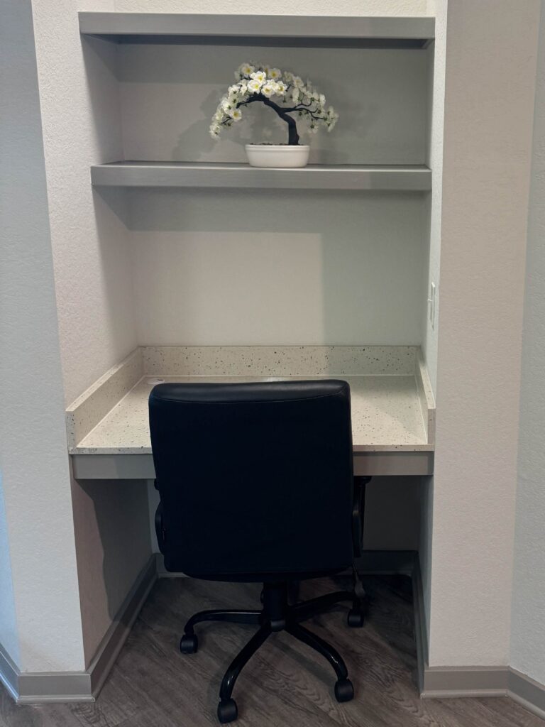 Compact built-in workspace with a desk nook, office chair, shelving, and decorative white floral arrangement.