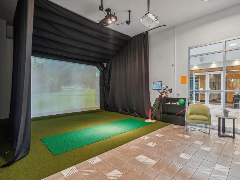 Indoor golf simulator room with projection screen, artificial turf, and seating area.