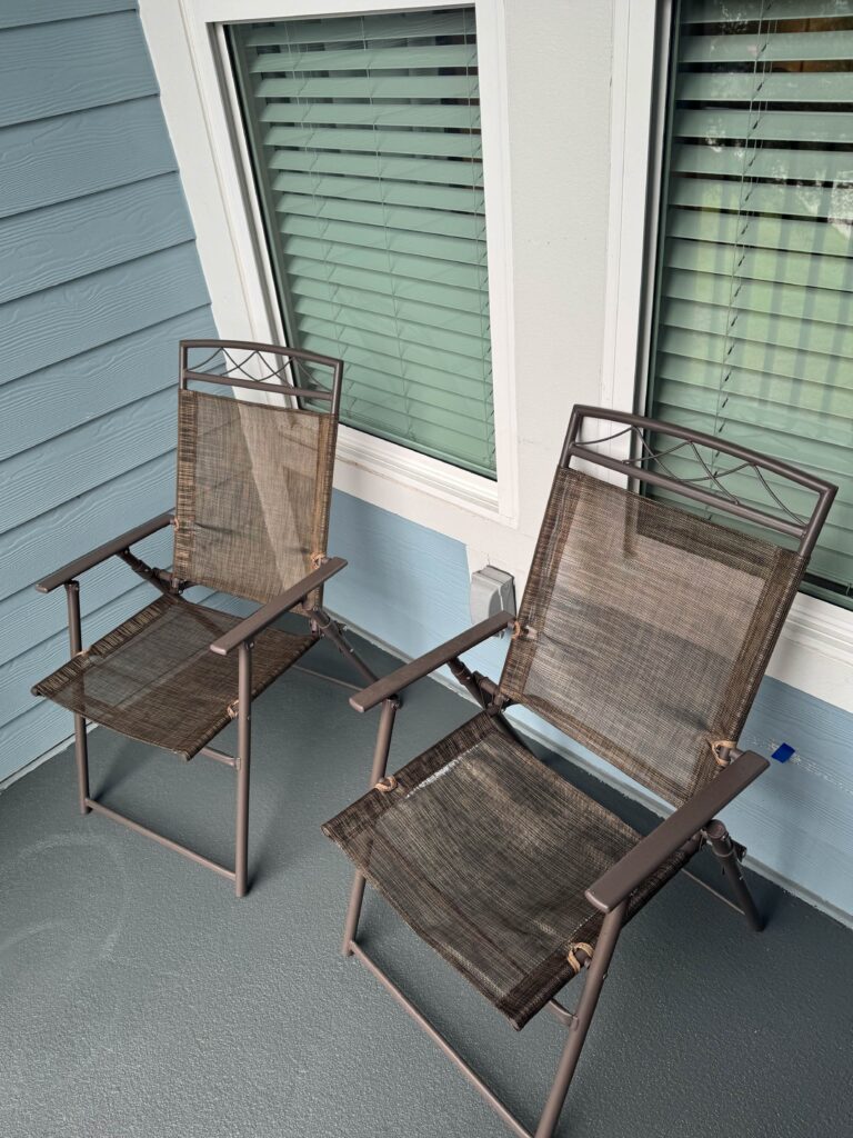 Private outdoor patio with two mesh patio chairs beside large windows and light blue exterior siding.
