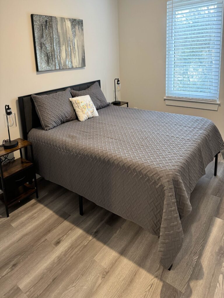 The primary bedroom at Legacy Townhomes offers a spacious and inviting retreat designed for rest and relaxation. Furnished with a comfortable king-size bed, coordinated bedside tables, and soft ambient lighting, the room creates a peaceful environment after a busy workday or travel schedule. Large windows allow natural light to fill the space while maintaining privacy, and the neutral color palette contributes to a calm, residential atmosphere. Ample room for luggage, personal belongings, and extended-stay living makes the bedroom especially well-suited for relocating professionals, traveling healthcare workers, project teams, and families. Combined with the townhome’s modern amenities and private residential setting, the primary suite provides the comfort and functionality guests expect from a true home away from home.