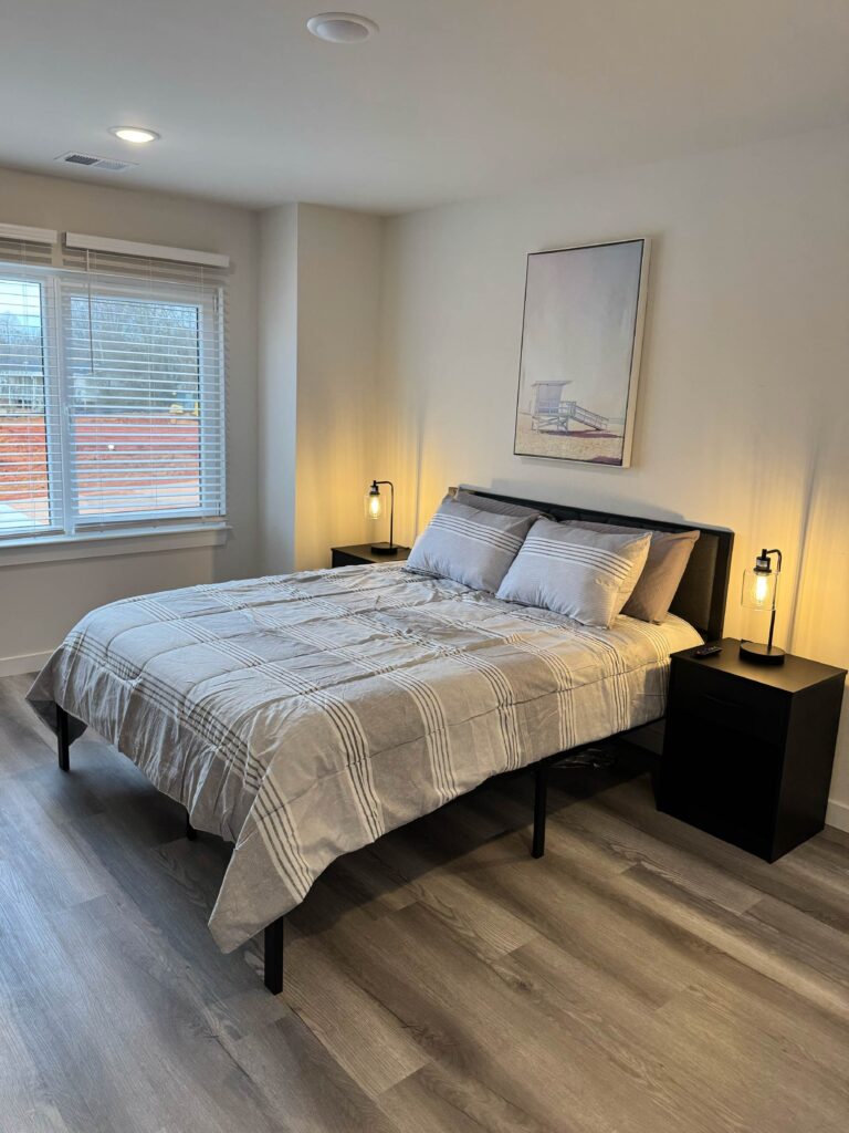 Spacious primary bedroom featuring a king-size bed, bedside tables with lamps, large windows, and contemporary furnishings.